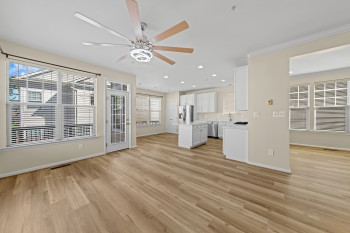 Wood-finish flooring, a modern ceiling fan with light, white kitchen cabinetry, a kitchen island, and stainless steel appliances