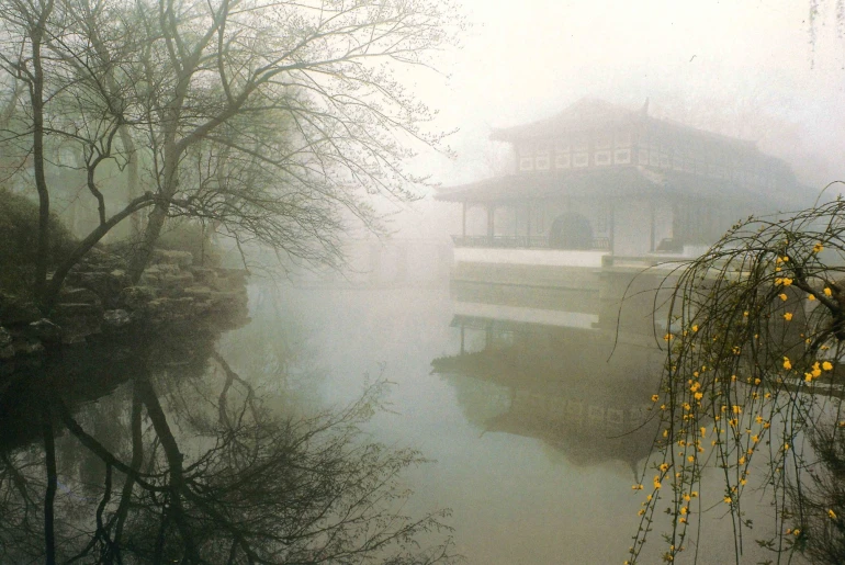 A serene scene of a foggy garden with a traditional pavilion beautifully reflected in a pond.