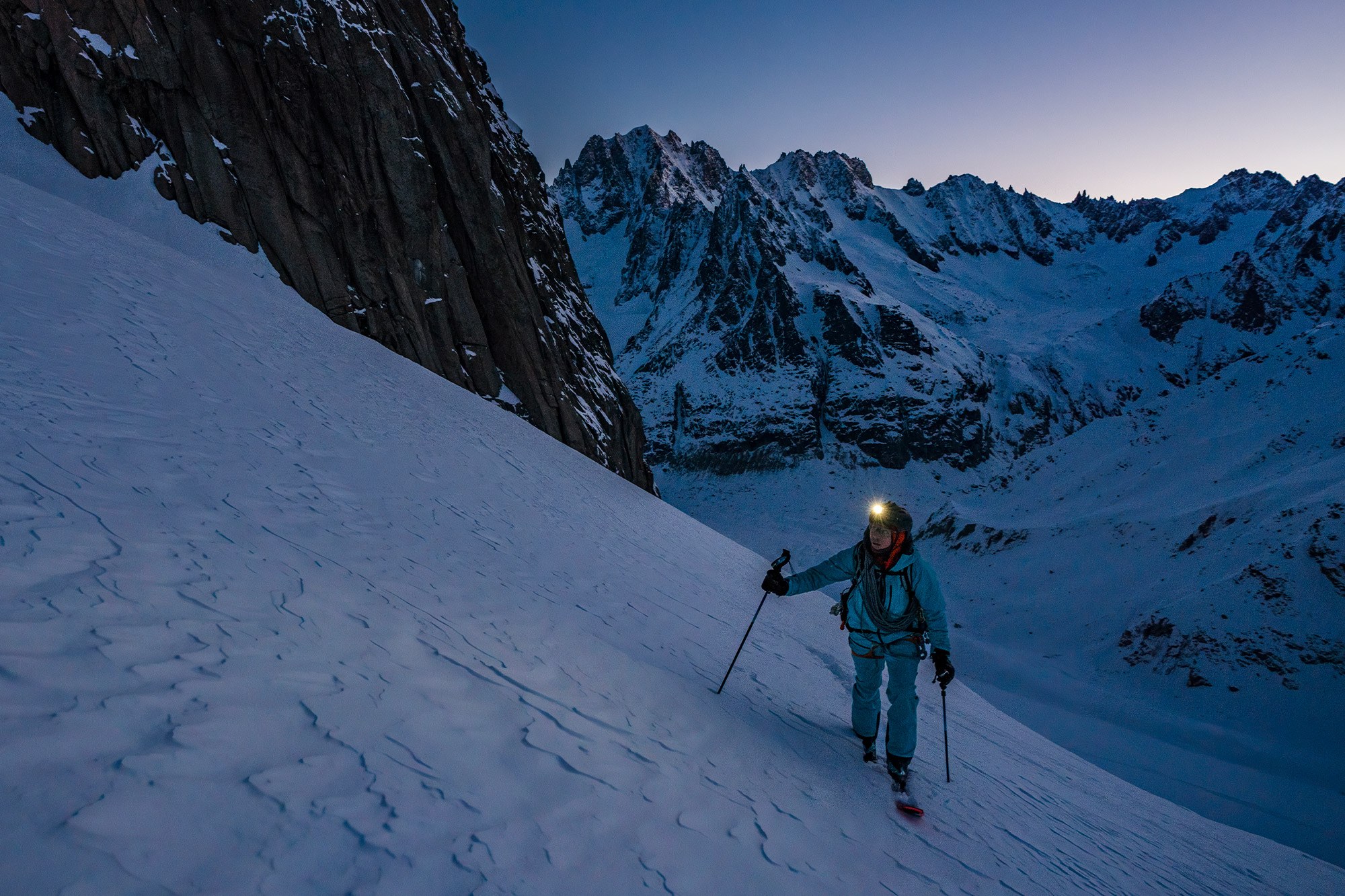 Vivian ascends a snowy slope at dawn with a headlamp