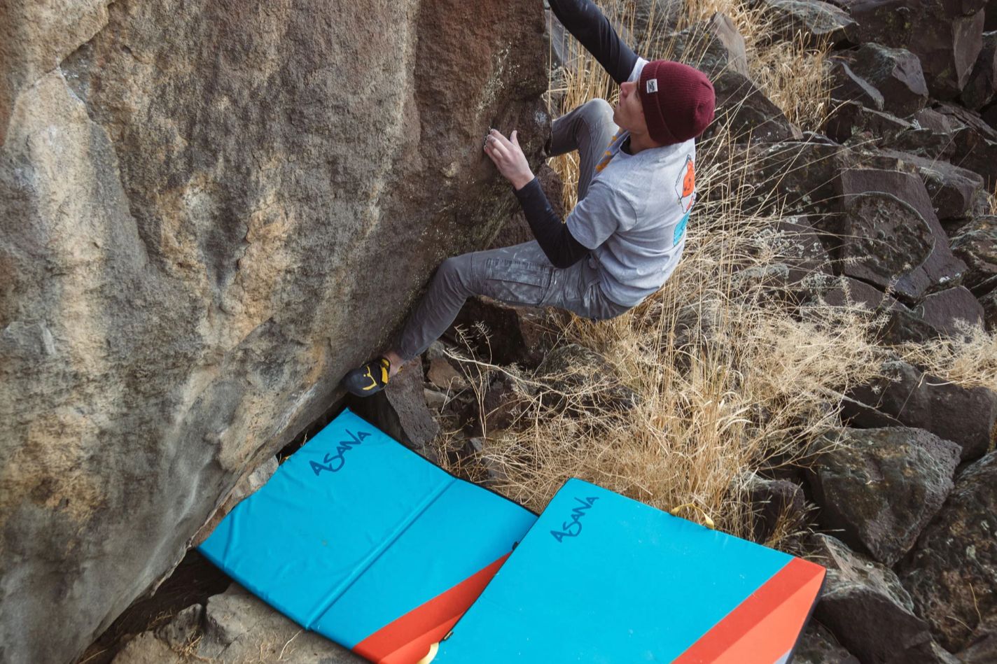 Boulderer climbing above two Asana crashpads.