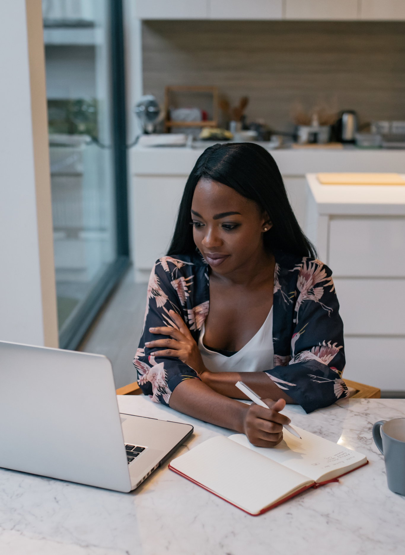 A single independent black african american woman working freelance from her luxurious apartment room on her laptop with a cup of coffee and note book 