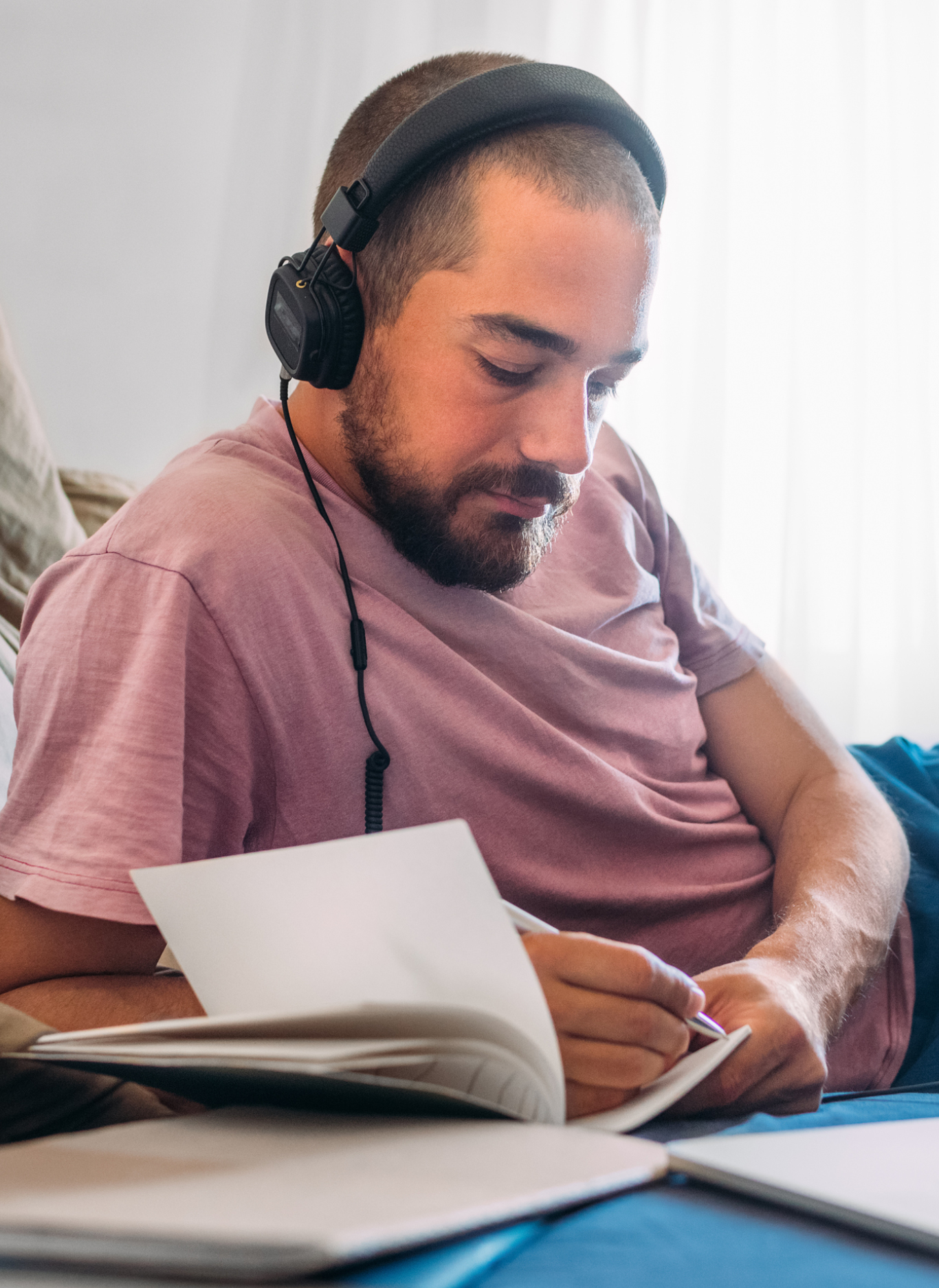 A fine-looking man spending day in his bedroom, listening to music, writing notes 