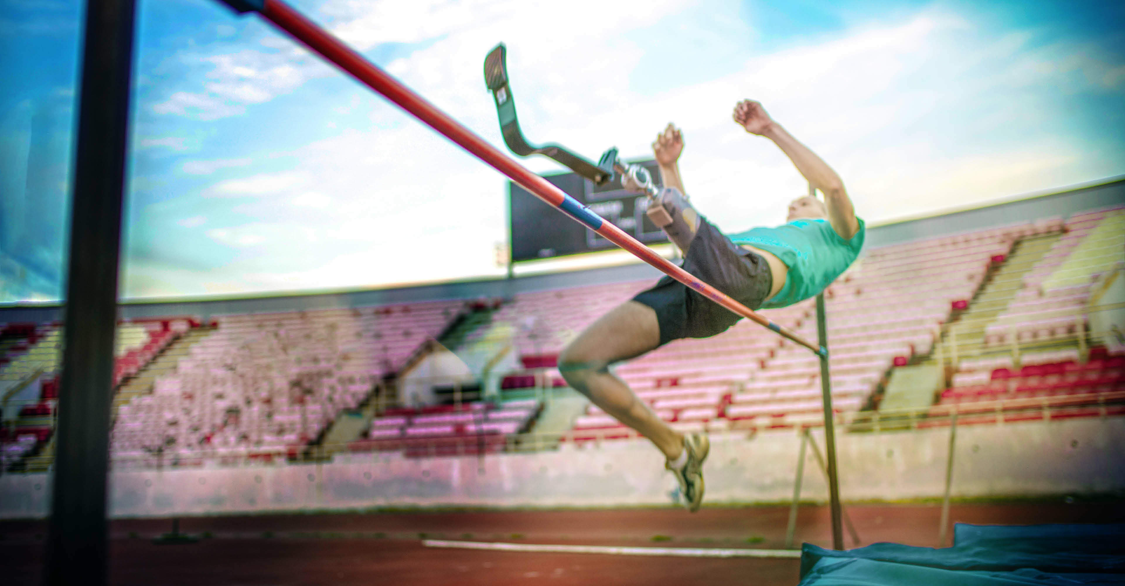 Man with a prosthetic leg jumping over a high jump bar for a track and field event