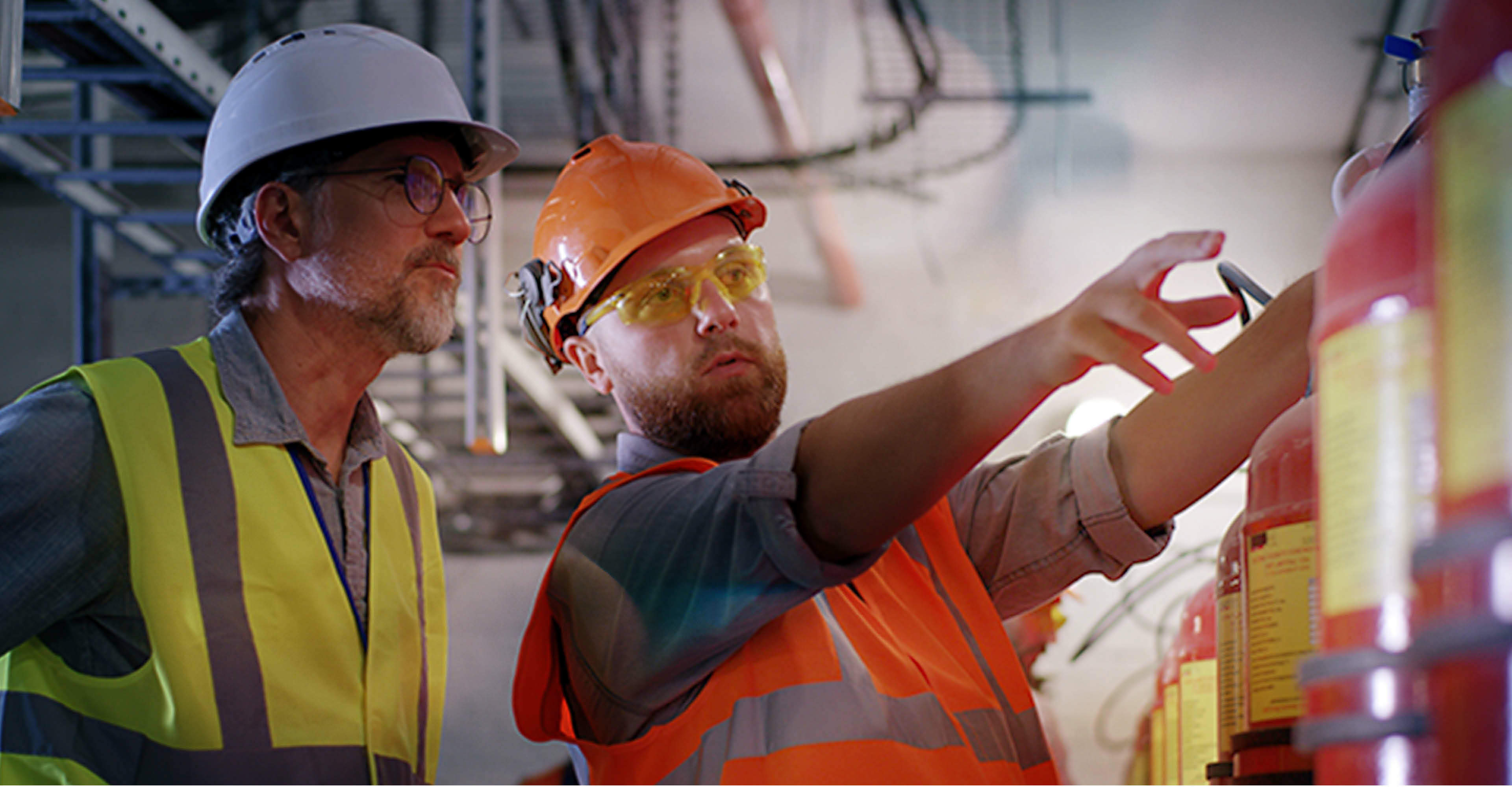 Bearded worker demonstrating fire extinguishers to mature inspector while working on power station