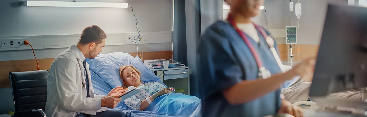 Female Head Nurse Uses Medical Computer, In the Background a Doctor is Consulting a Patient