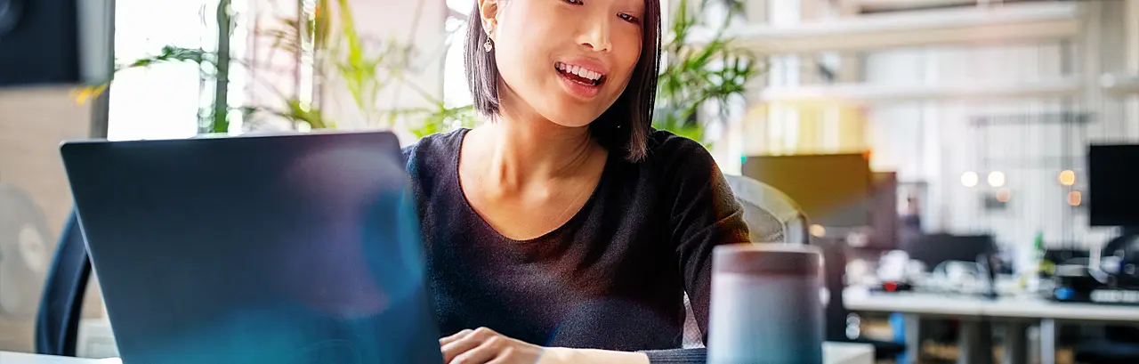  Female professional working on laptop and talking into a speaker.