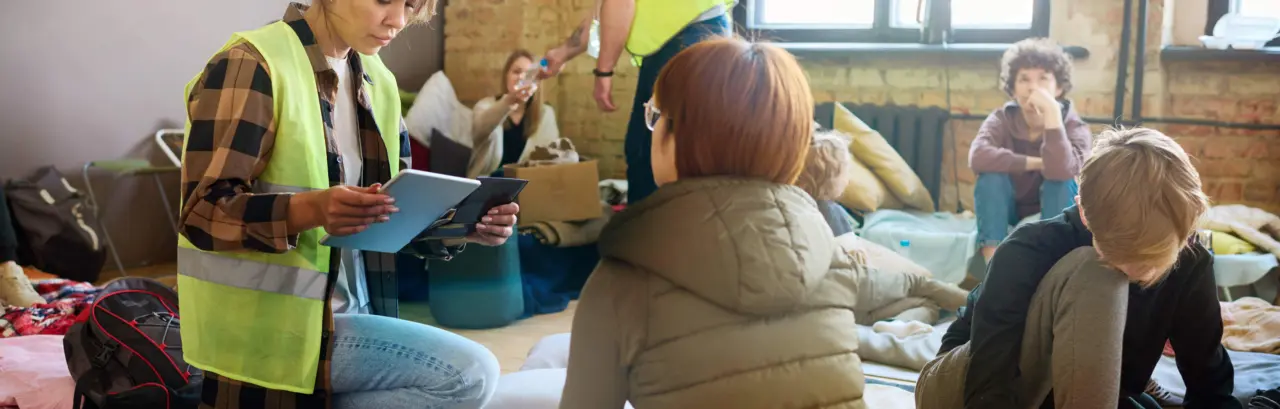 Female volunteer with mobile gadgets sitting on squats in front of refugee
