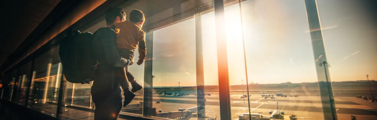 Father and young son watching planes on the tarmac inside a passenger terminal,