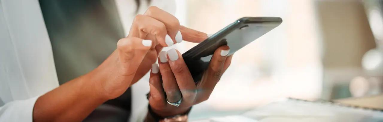 woman at desk with laptop, holding and using her smartphone