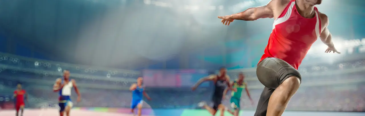 Male track athlete sprinting over the finish line of a race with his arms outstretched in victory