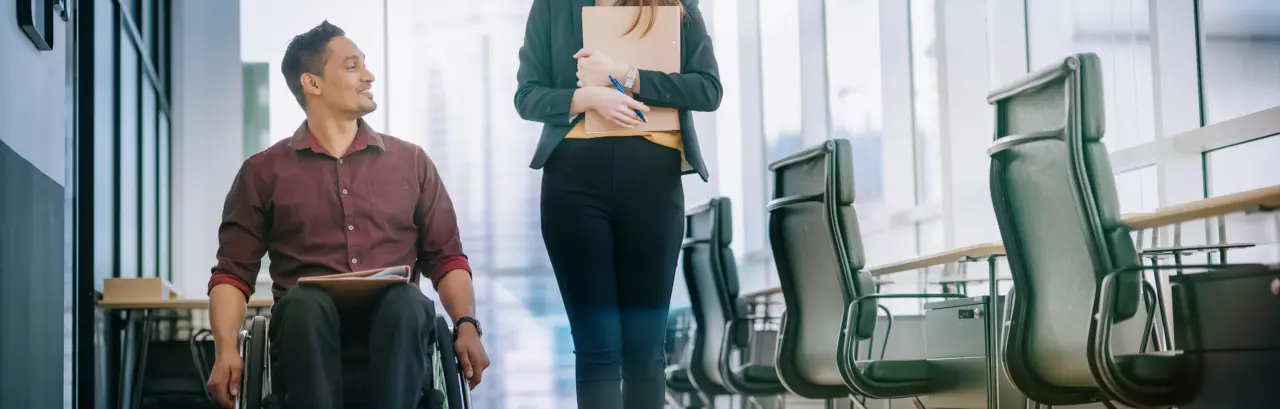 male worker in wheelchair having conversation with his female colleague as they move down the hall