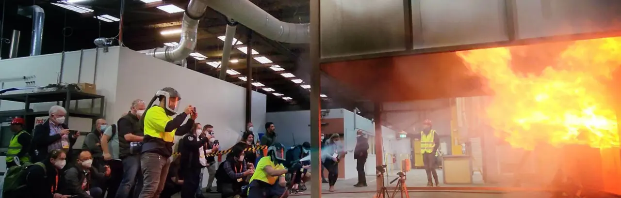 Fire test being conducted in a burn room. Multiple people in protective equipment are watching.