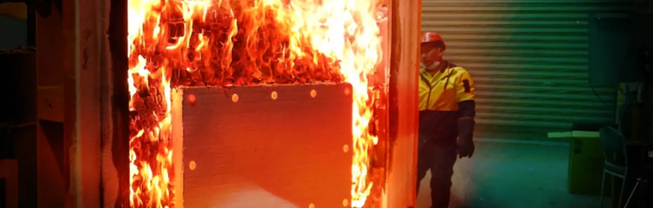Fire resistance test conducted in a laboratory. Man in protective equipment in the background.