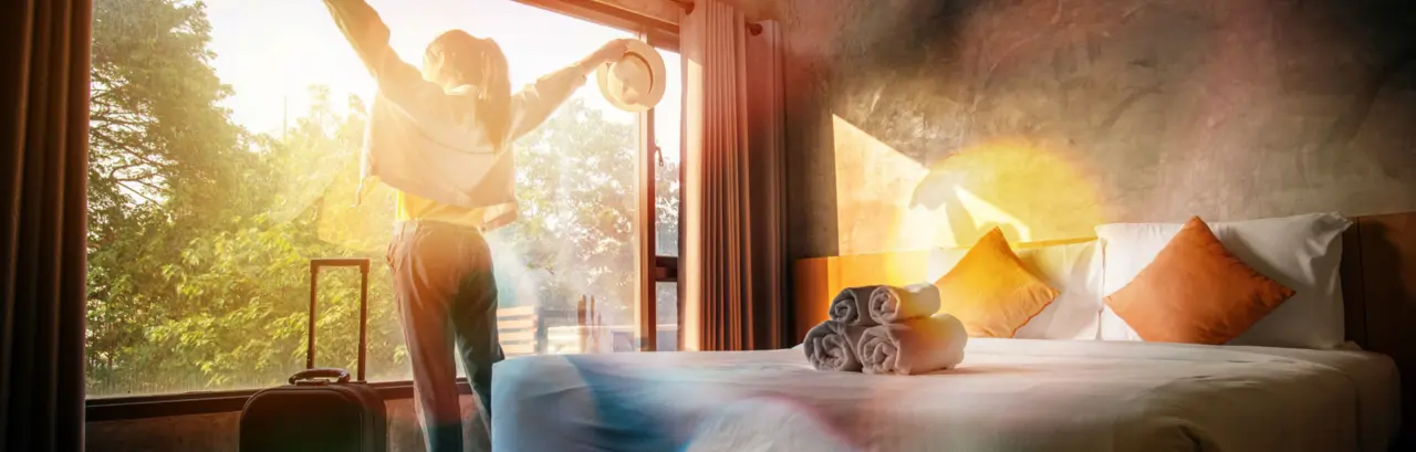 Portrait of tourist woman raised her hands and standing near a window, looking to beautiful view