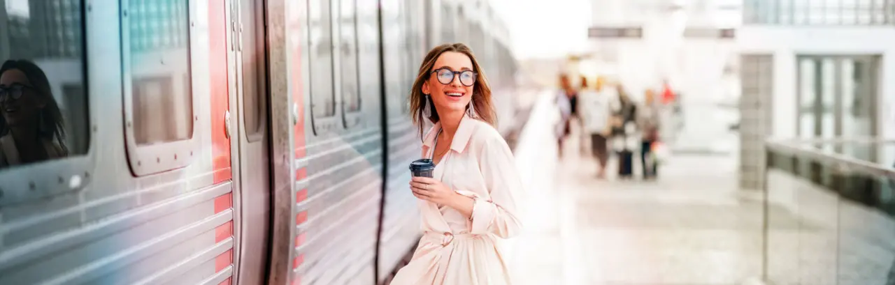 Young and beautiful woman with coffee cup boarding in the train at the modern railway station