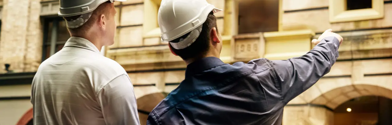 Two engineers in white hard hats pointing at a building