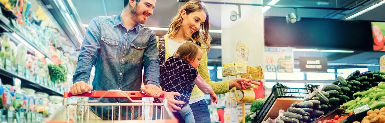 Happy couple with a baby pushing a shopping cart in a grocery store