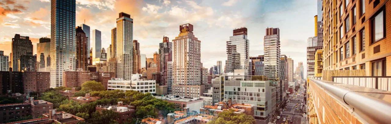 Wide-angle view of New York skyline with tall buildings, a tree-filled park, and a busy street