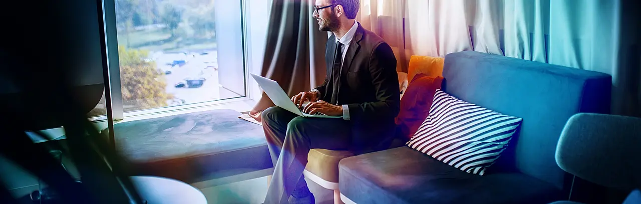 businessman in suit and with eyeglasses sitting in office on sofa, holding laptop in lap