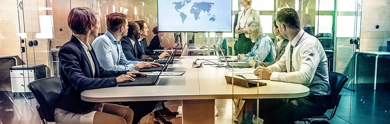 Group of businesspeople sitting at a table in a glass conference room during a presentation