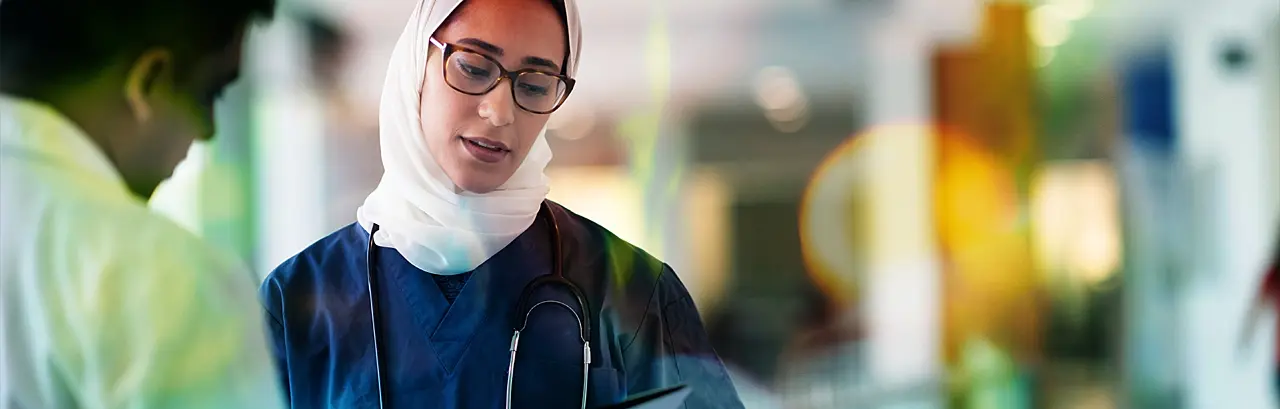 Two medical professionals are meeting casually in a hospital corridor holding folders