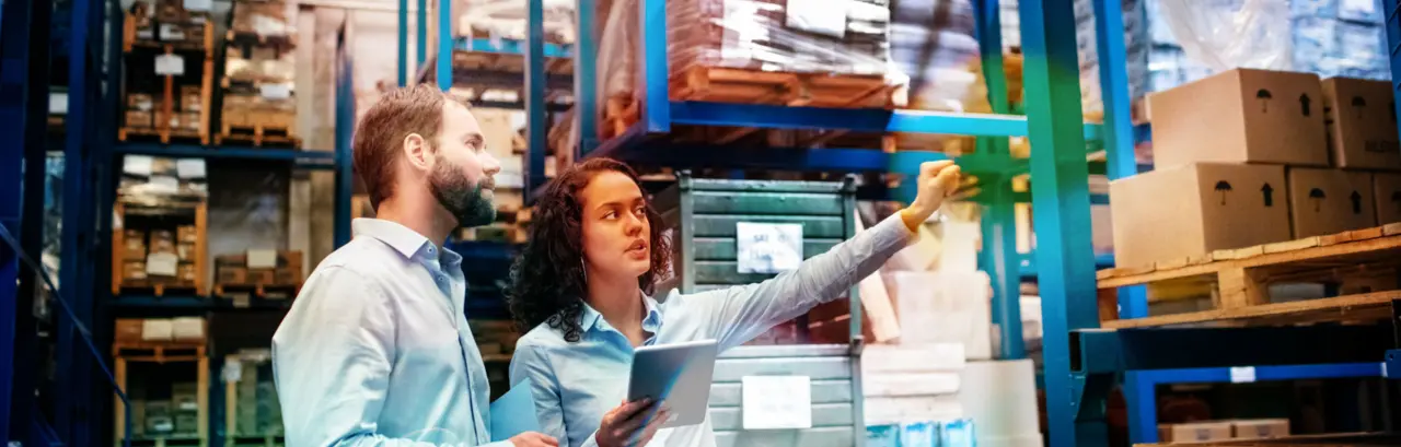 Businesswoman with a digital tablet showing and talking with male worker in distribution warehouse