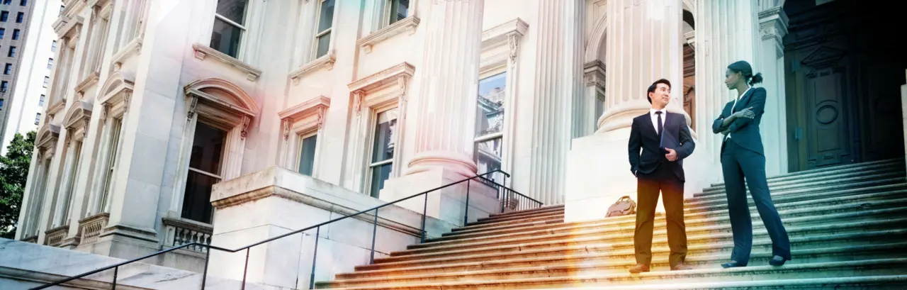 A well dressed man and woman converse on the steps of a legal or municipal building.