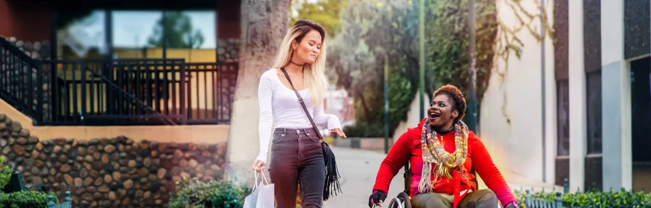 A young black disabled woman with a wheelchair and a bright sweater and her Asian friend walking.