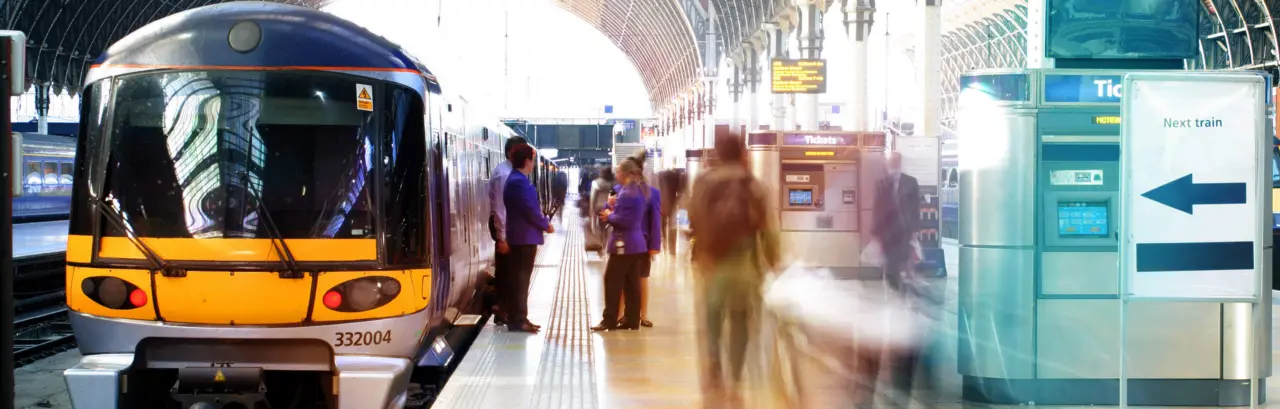 A train at a train station. Blurred station staff and commuters on the platform.