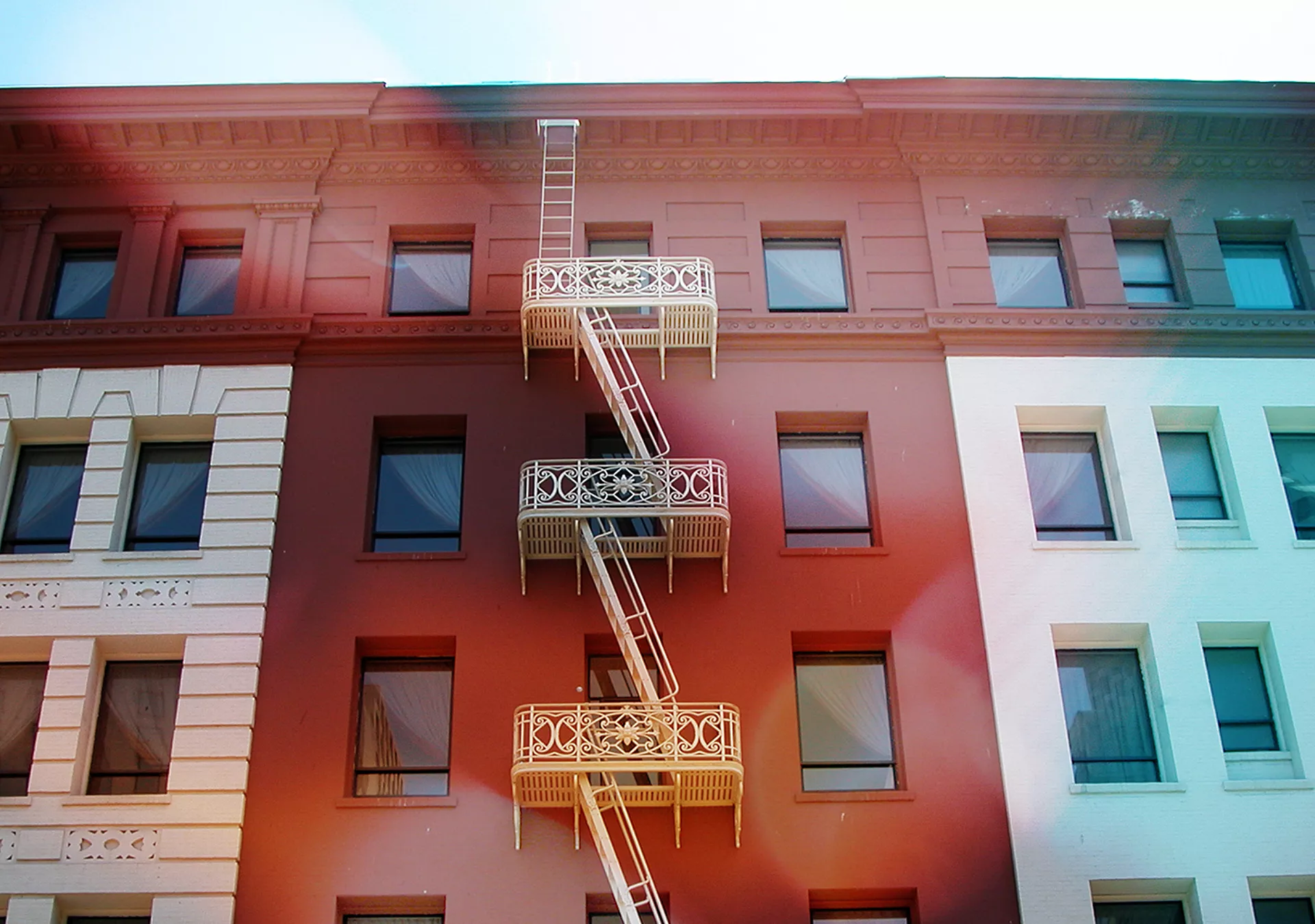 A white fire escape stands out against the red section of a building it snakes up