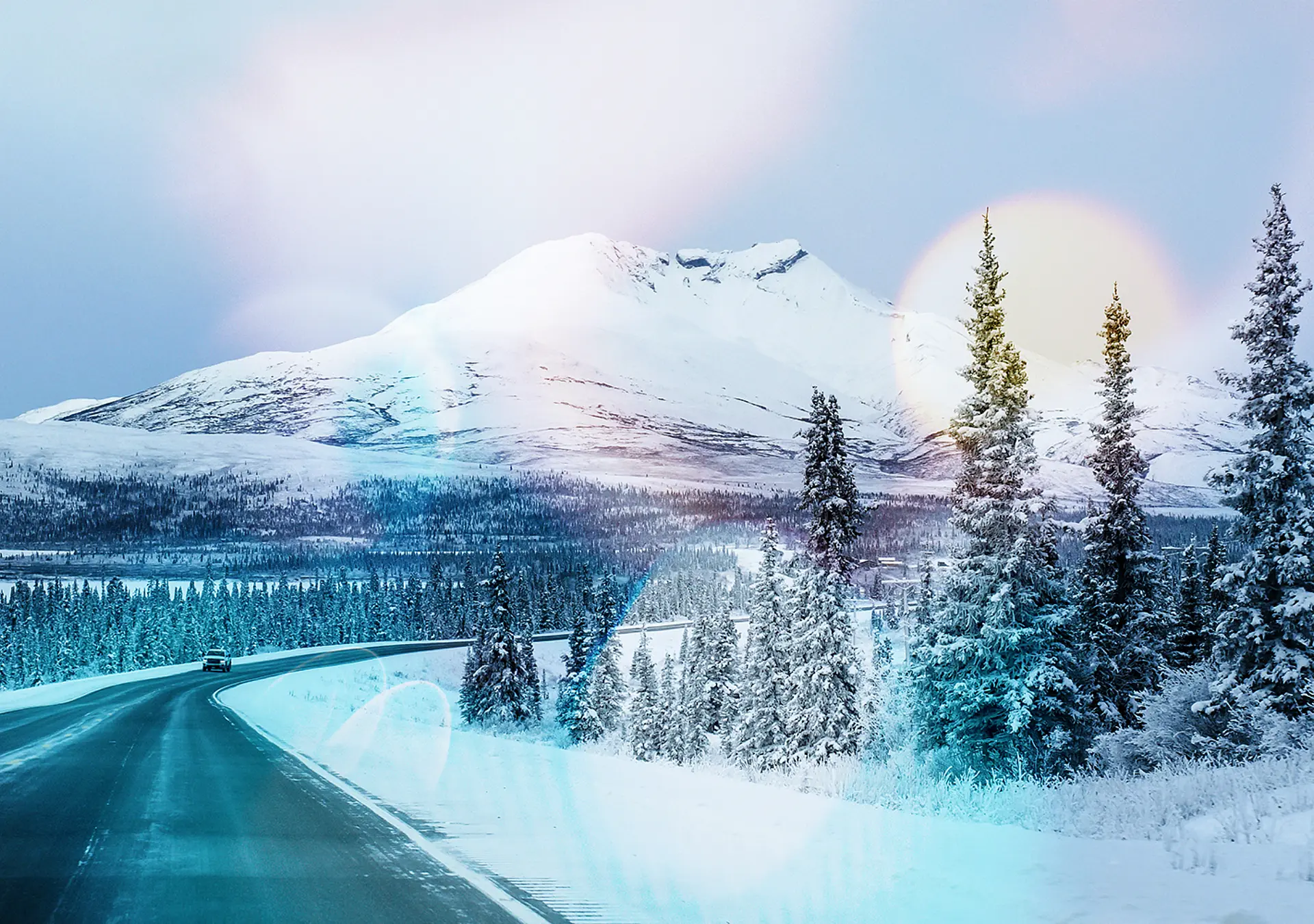 Snow-covered trees surround the highway with a snow-capped mountain in the background