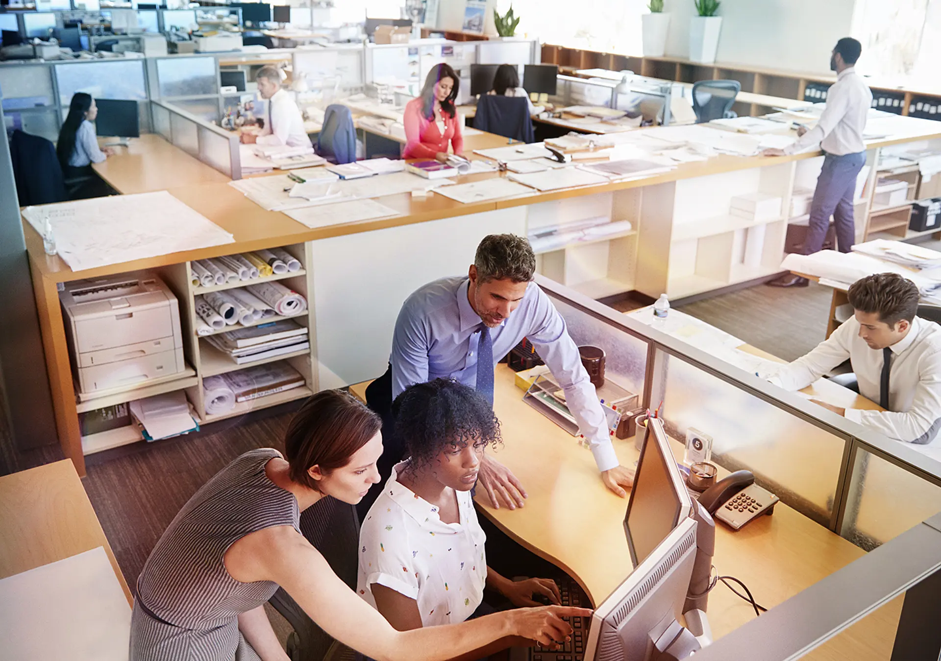 Colleagues working at a woman's workstation in a busy office