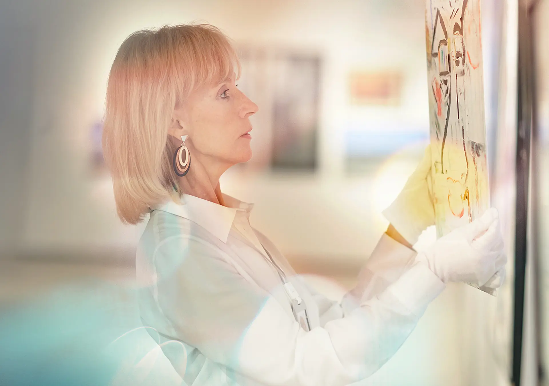 Side view portrait of elegant mature woman hanging paintings while working in modern art gallery