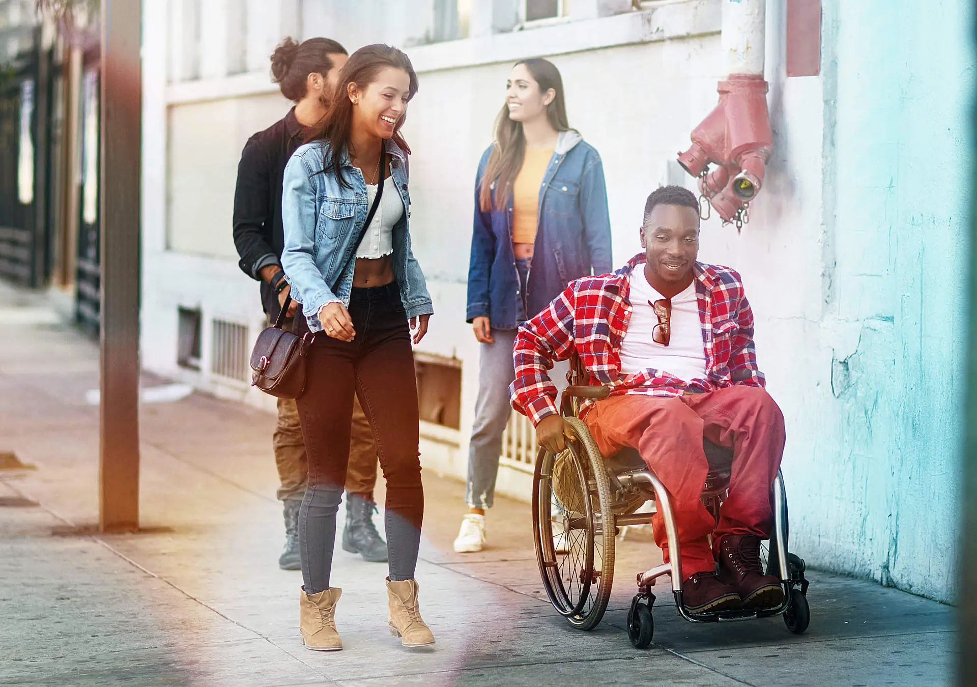 People walking with their male friend in a wheelchair on a city sidewalk wearing casual clothes