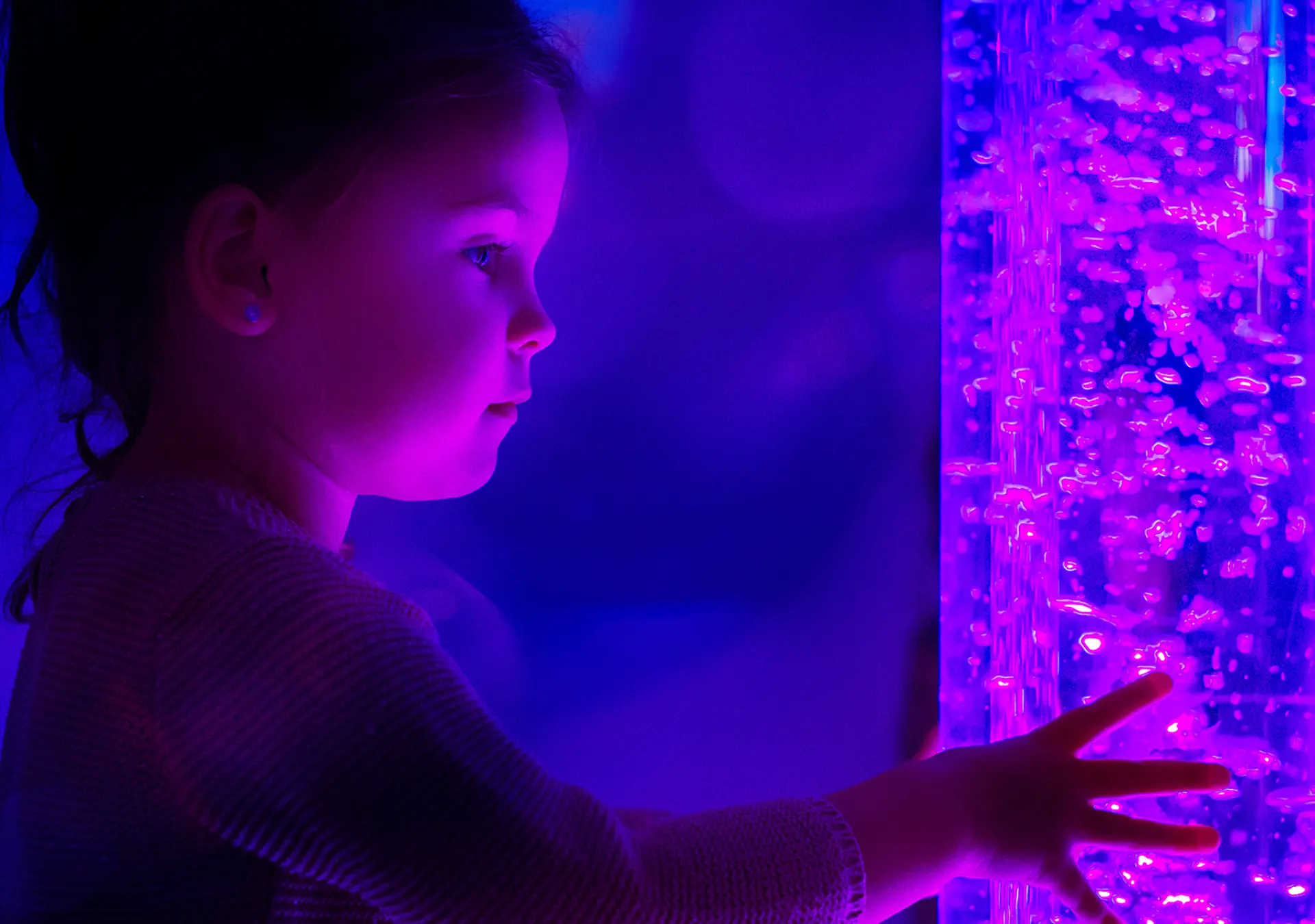 Child in therapy sensory stimulating room interacting with colored lights bubble tube