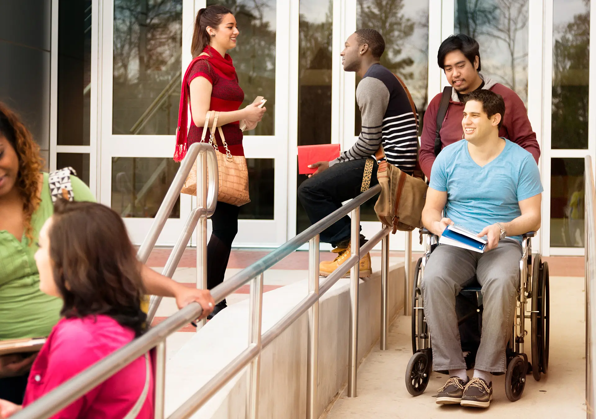 Wheelchair-bound college student is helped down the ramp by a friend or volunteer.