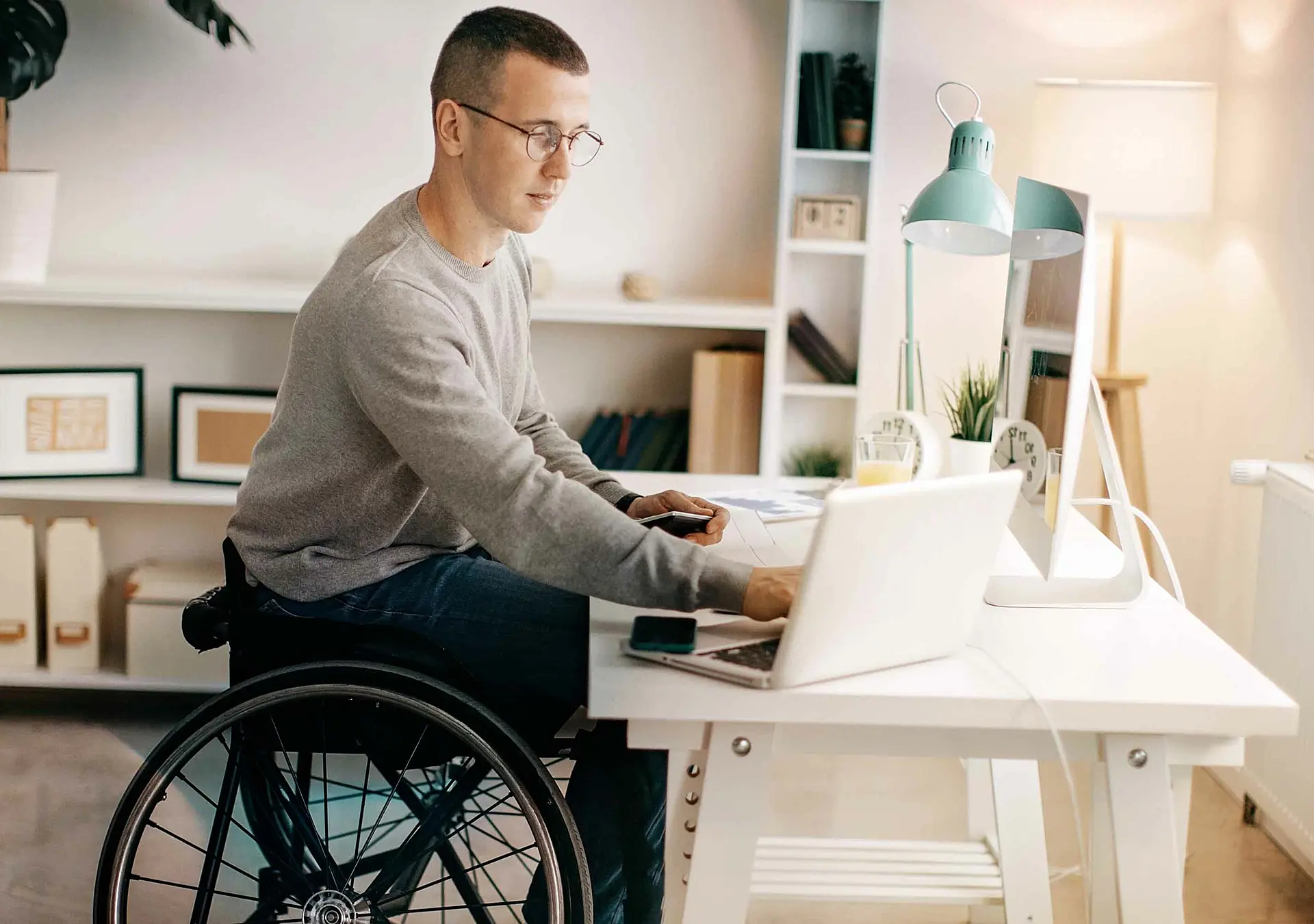 Young man in a wheelchair working on his laptop at his desk