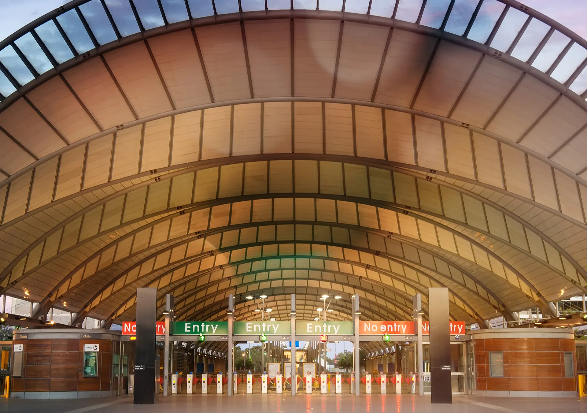 The modern train station at Sydney Olympic Park, seen at dusk under a colourful sky.
