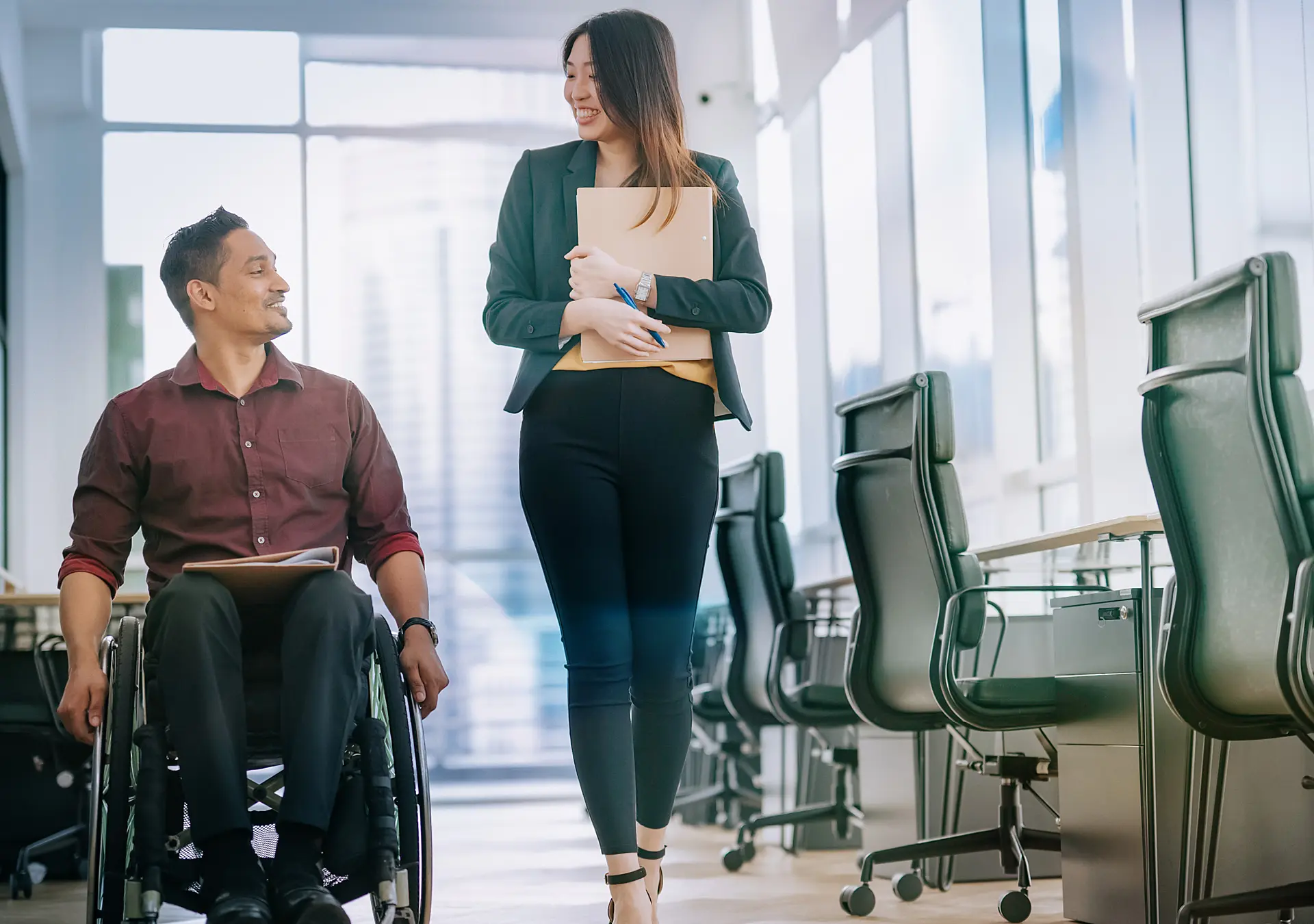 male worker in wheelchair having conversation with his female colleague as they move down the hall