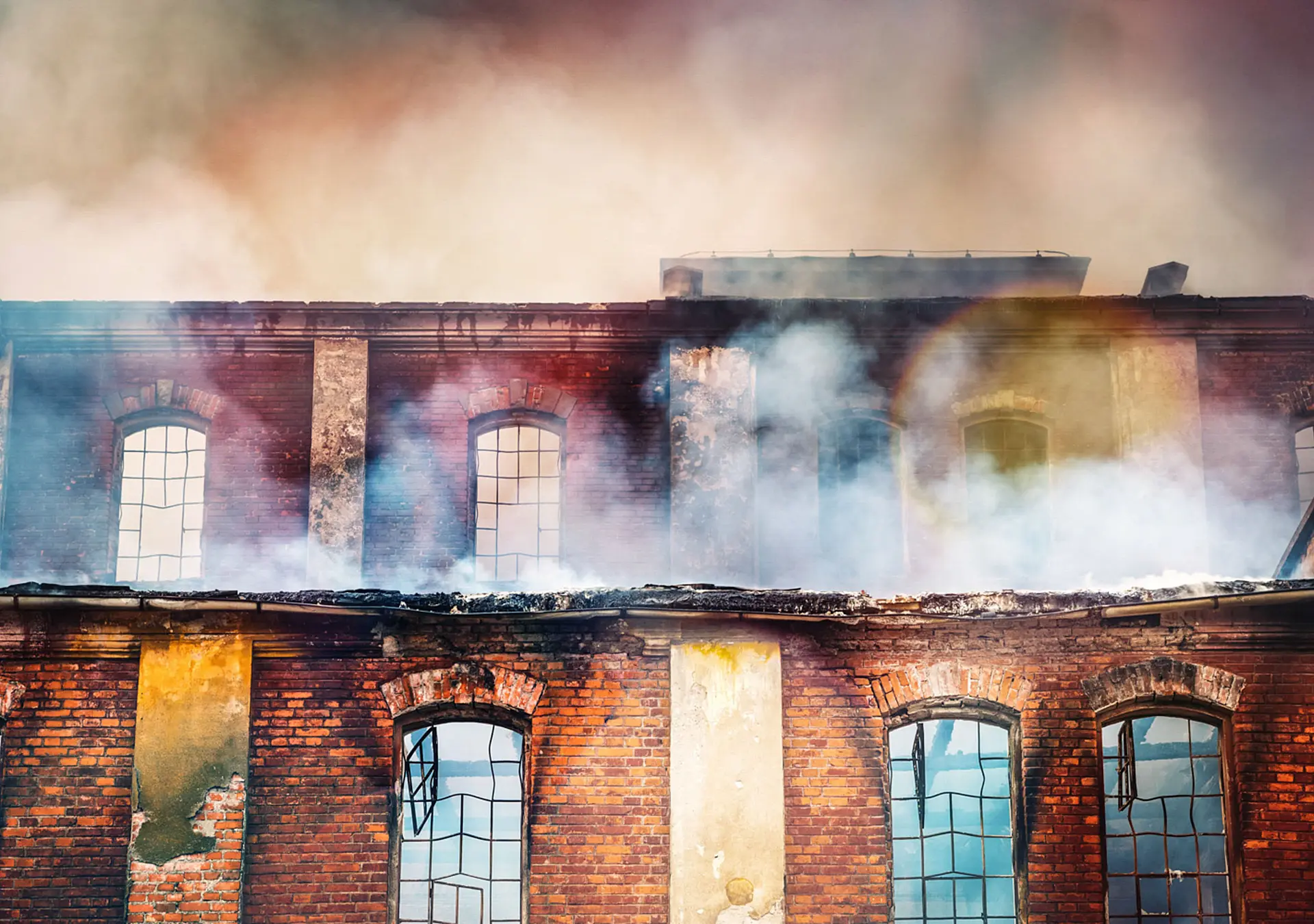 Photo of a burning old red-brick factory with a lot of smoke.