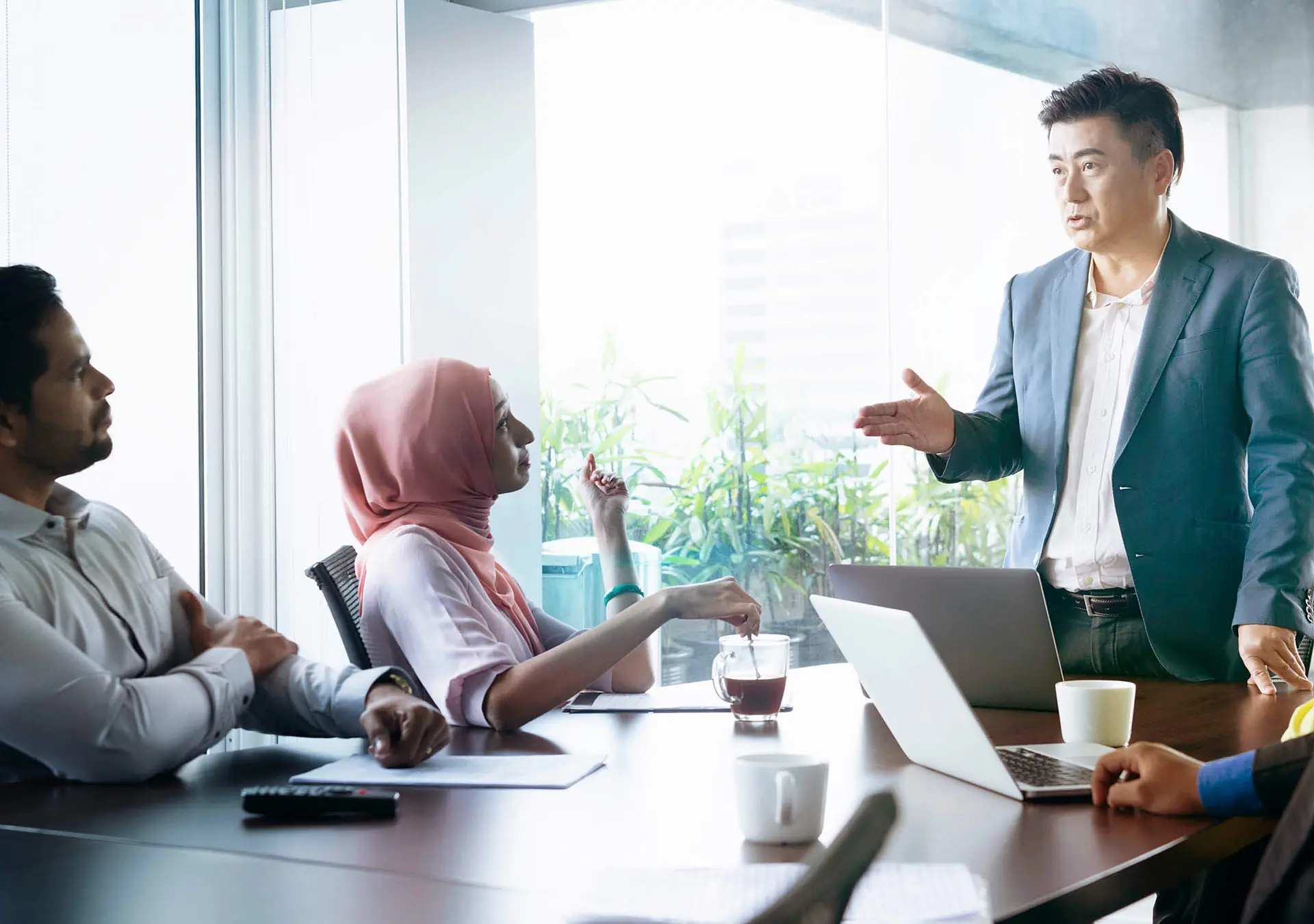 Multi racial group of business people sitting around meeting table and listening to male manager