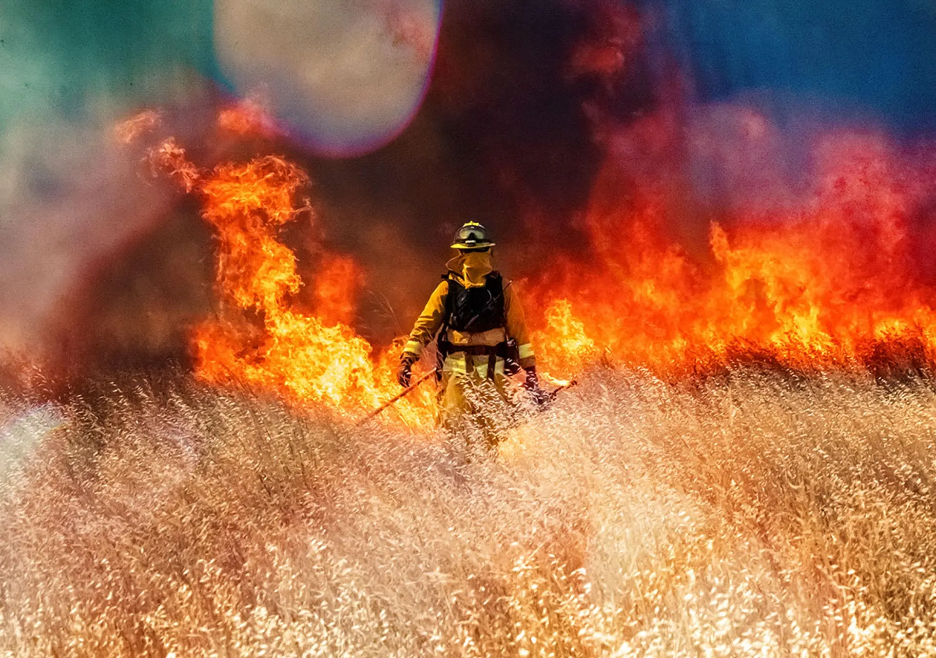 Wildfire raging across grass meadow in California, firefighter walking through meadow