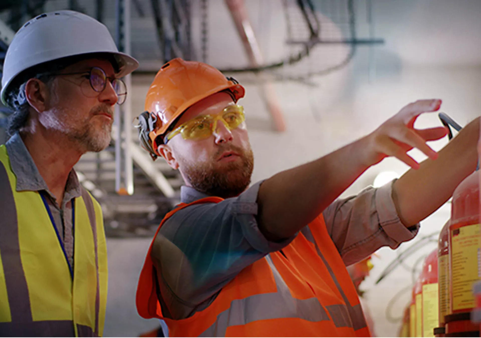 Bearded worker demonstrating fire extinguishers to mature inspector while working on power station