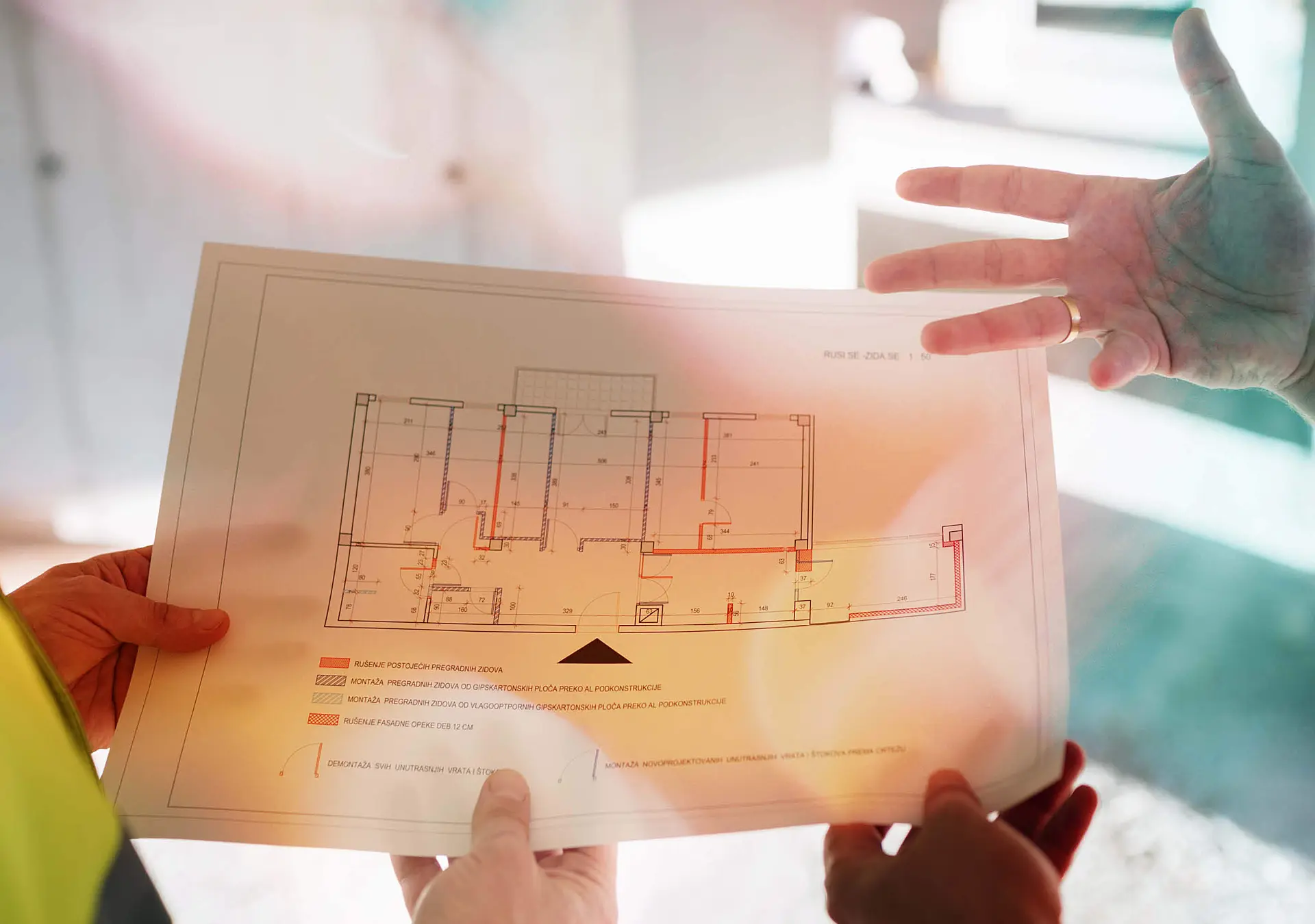 Two people review a building floor plan drawing at a construction site, with hands gesturing .