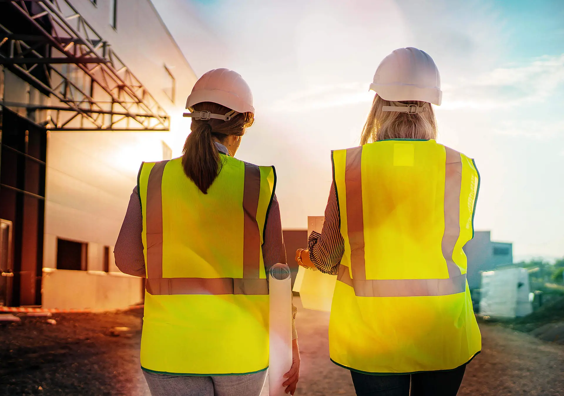 Two women, both in hard hats, walk side by side in front of a building
