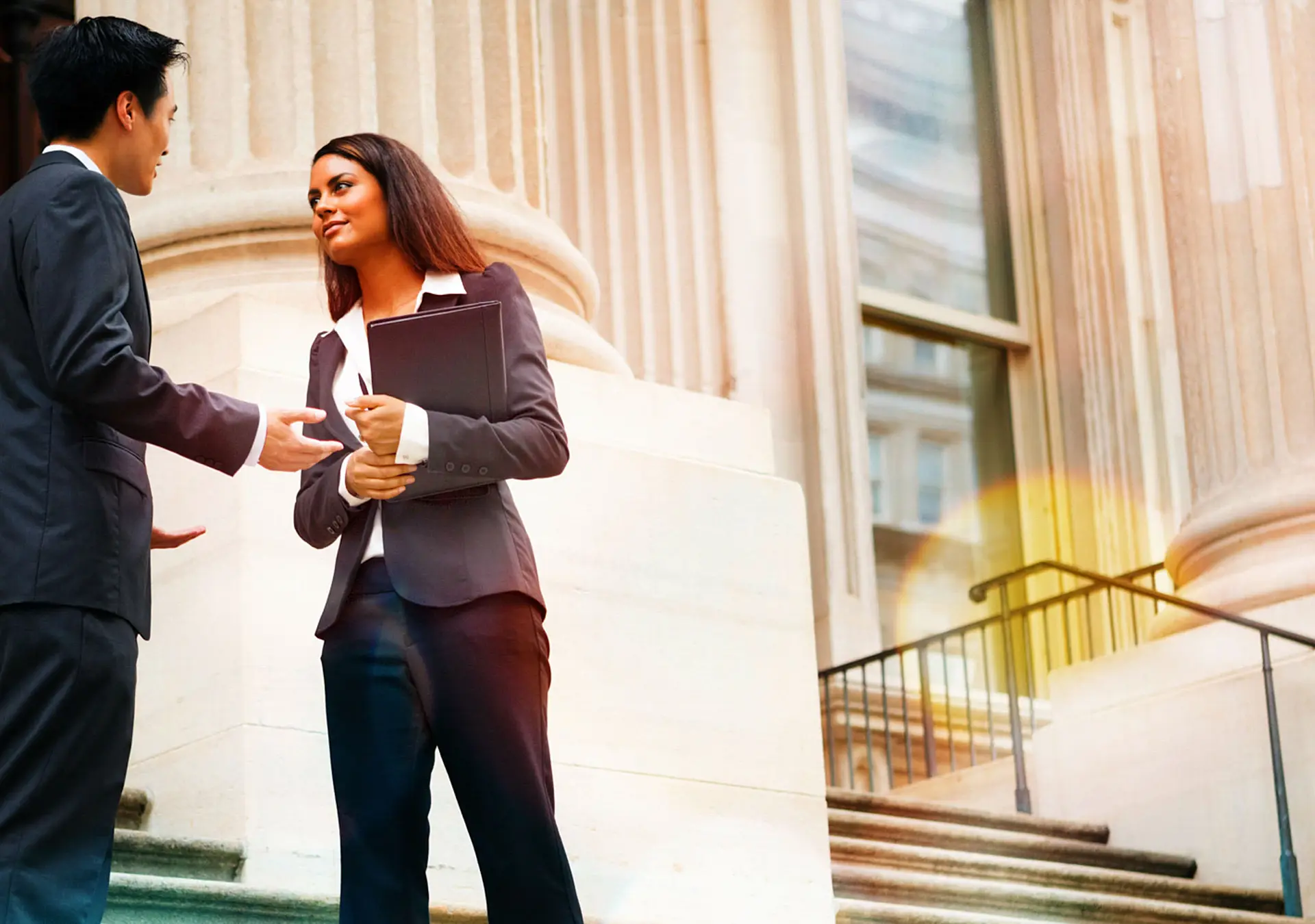 Professional woman and man having a discussion on the stairs of a stately building.
