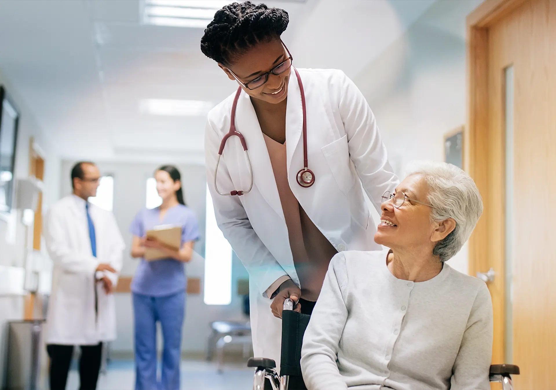 A female doctor pushing a senior patient on a wheelchair in a hospital, smiling at each other