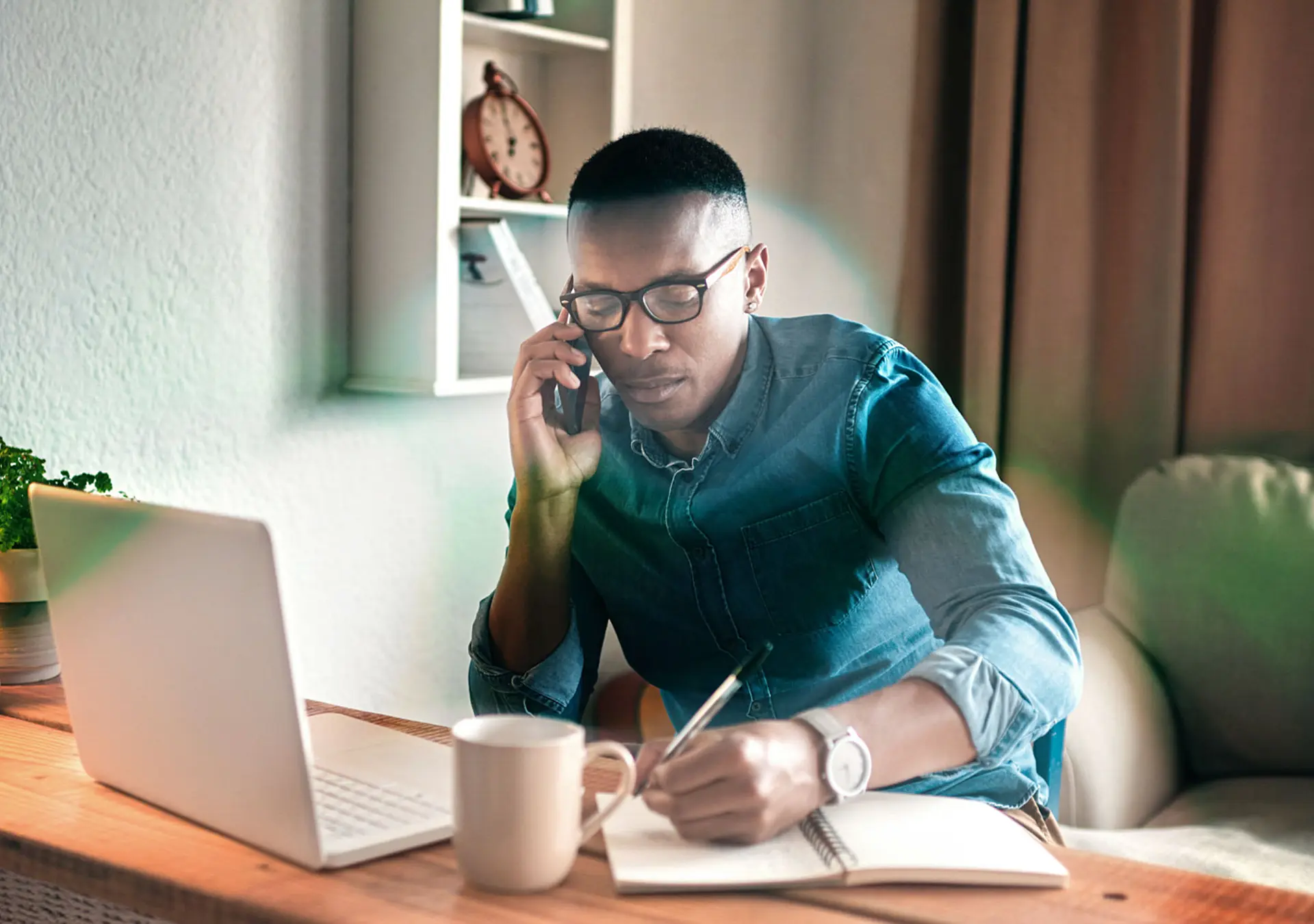 young businessman sitting alone in his office and talking on his cellphone while making notes