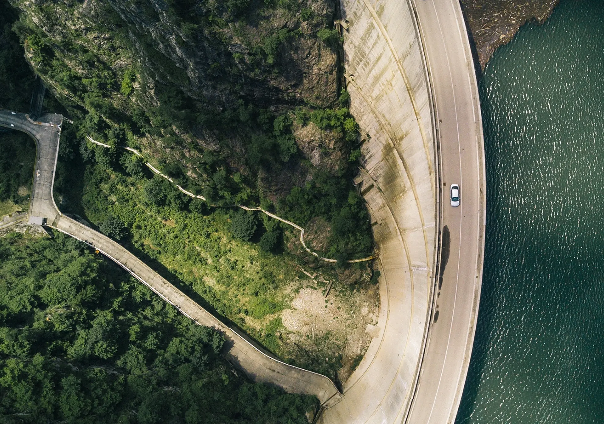 Aerial shot of a road that is next to a body of water and some foliage