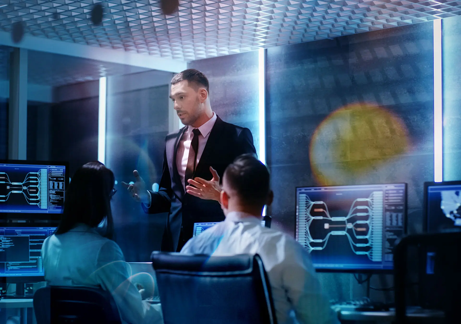 Supervisor Holds Briefing for His Employees in System Control Center Full of Monitors and Servers.